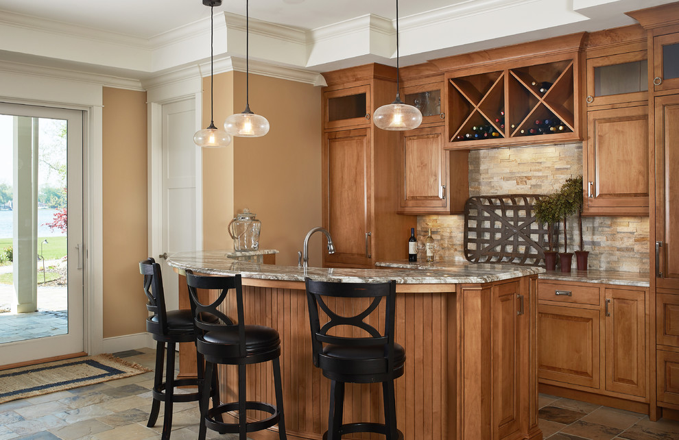 Home bar - traditional ceramic tile and brown floor home bar idea in Grand Rapids with flat-panel cabinets, medium tone wood cabinets, granite countertops, beige backsplash, stone tile backsplash and multicolored countertops