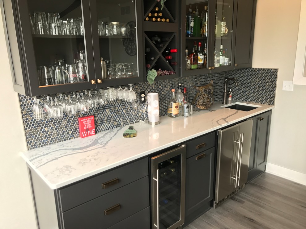 Medium sized contemporary single-wall wet bar in Other with a submerged sink, recessed-panel cabinets, black cabinets, engineered stone countertops, blue splashback, metal splashback, vinyl flooring and grey floors.