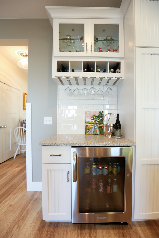 Small transitional single-wall medium tone wood floor wet bar photo in Other with no sink, recessed-panel cabinets, white cabinets, granite countertops, white backsplash and subway tile backsplash