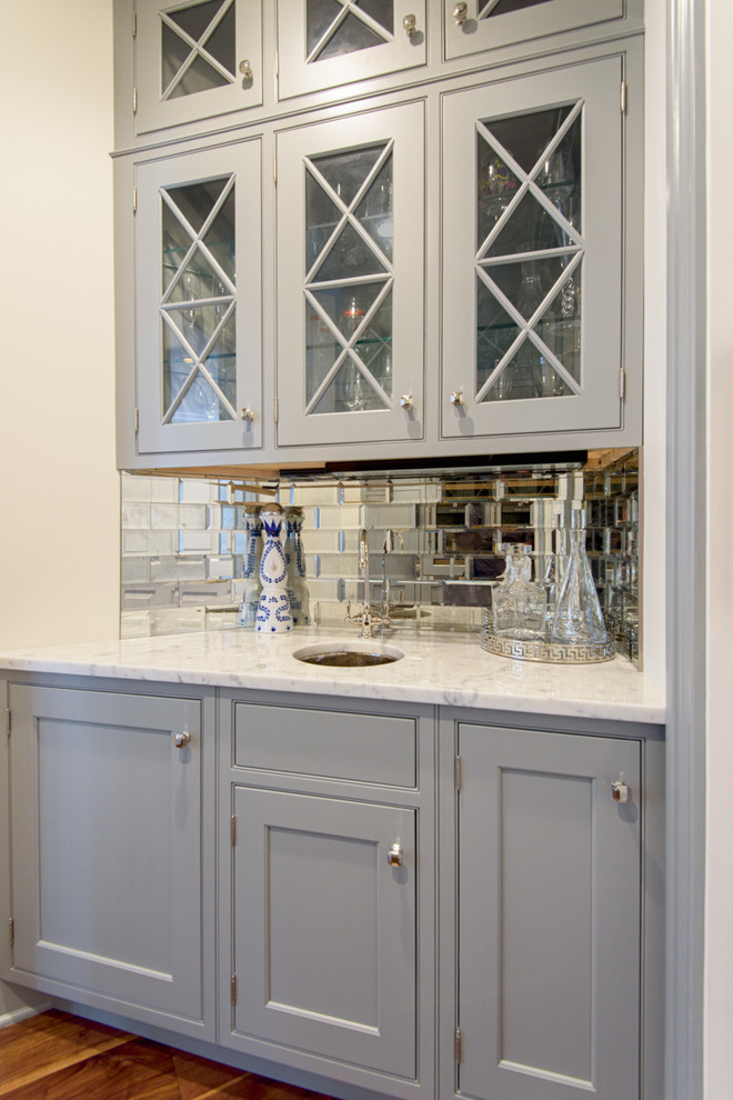This is an example of a small classic single-wall wet bar in New York with a submerged sink, glass-front cabinets, grey cabinets, marble worktops, metro tiled splashback and dark hardwood flooring.