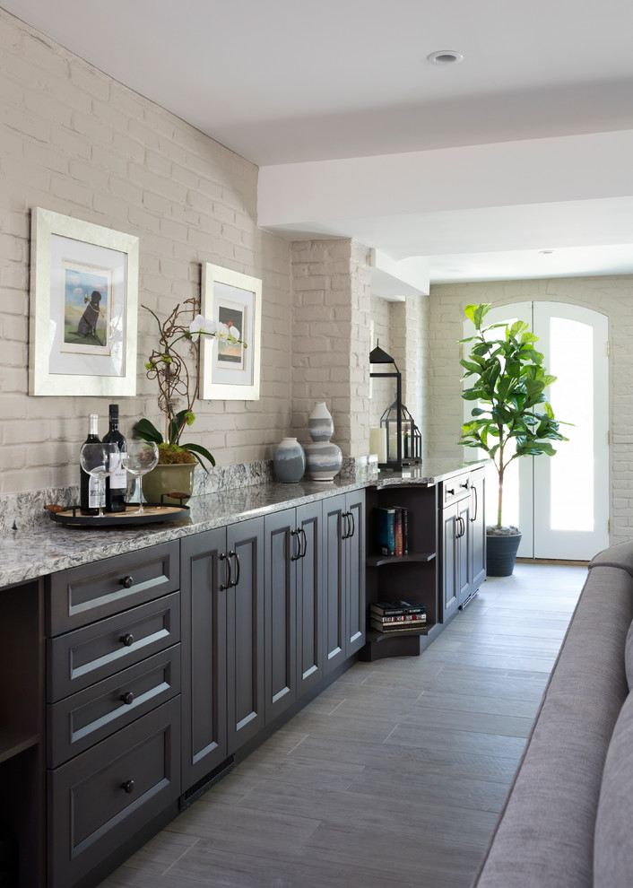 Klassisk inredning av en mellanstor linjär hemmabar med vask, med granitbänkskiva, vitt stänkskydd, stänkskydd i tegel, grått golv, luckor med infälld panel och heltäckningsmatta