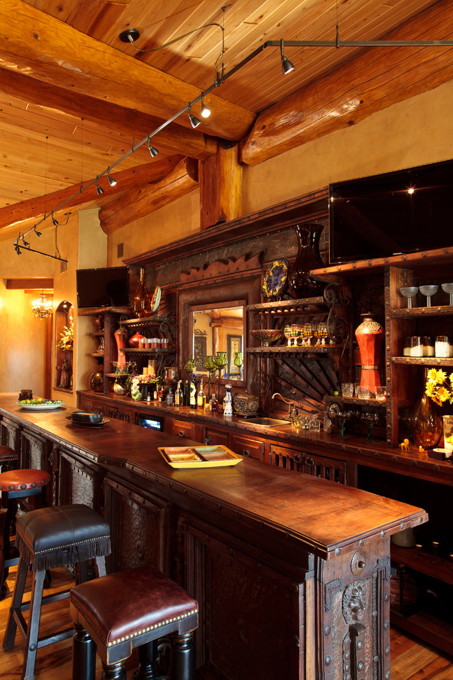 На фото: большой параллельный домашний бар в стиле рустика с барной стойкой, темными деревянными фасадами, деревянной столешницей, темным паркетным полом и коричневой столешницей с