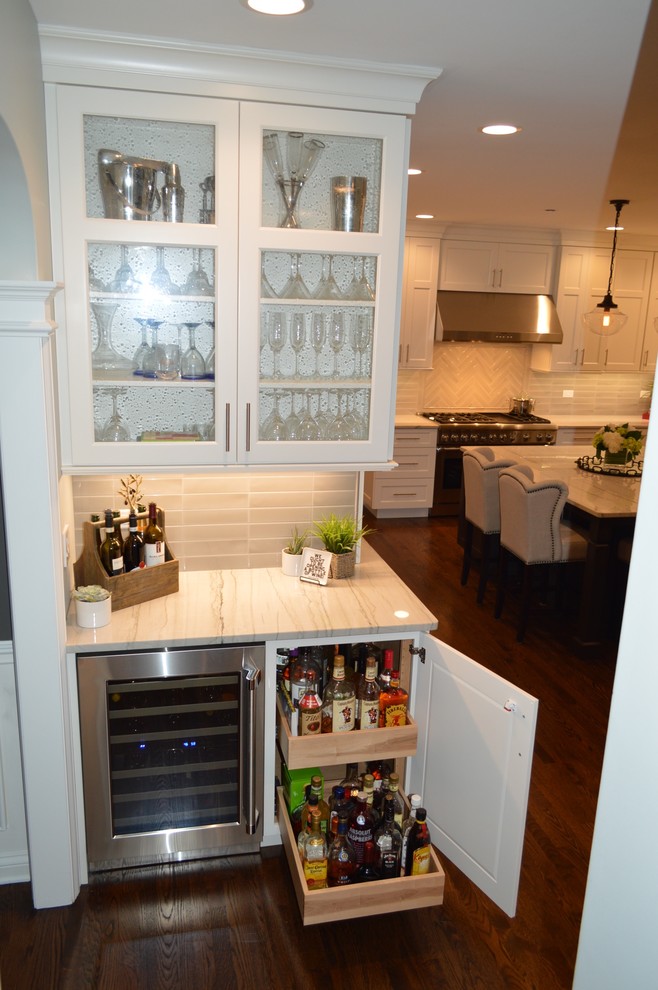 Cette photo montre un petit bar de salon linéaire chic avec aucun évier ou lavabo, un placard à porte vitrée, des portes de placard blanches, un plan de travail en quartz, une crédence grise, une crédence en carreau de verre, un sol en bois brun et un sol marron.