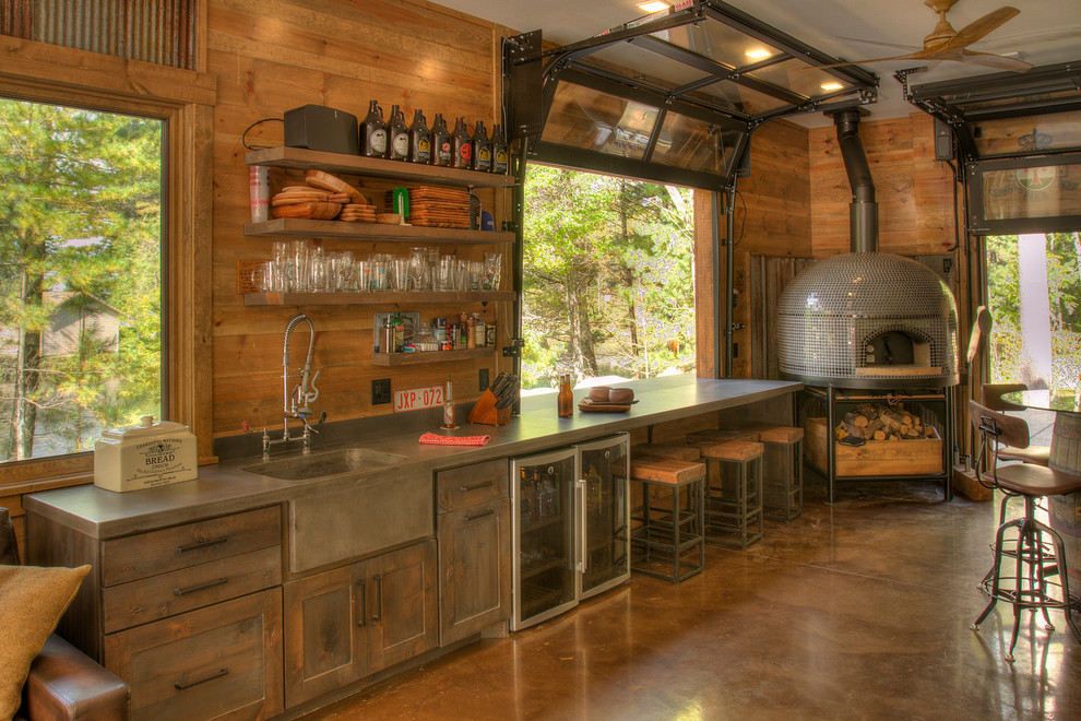 Diseño de bar en casa lineal rural con fregadero integrado, armarios estilo shaker, puertas de armario de madera en tonos medios, suelo de cemento, suelo marrón y encimeras grises