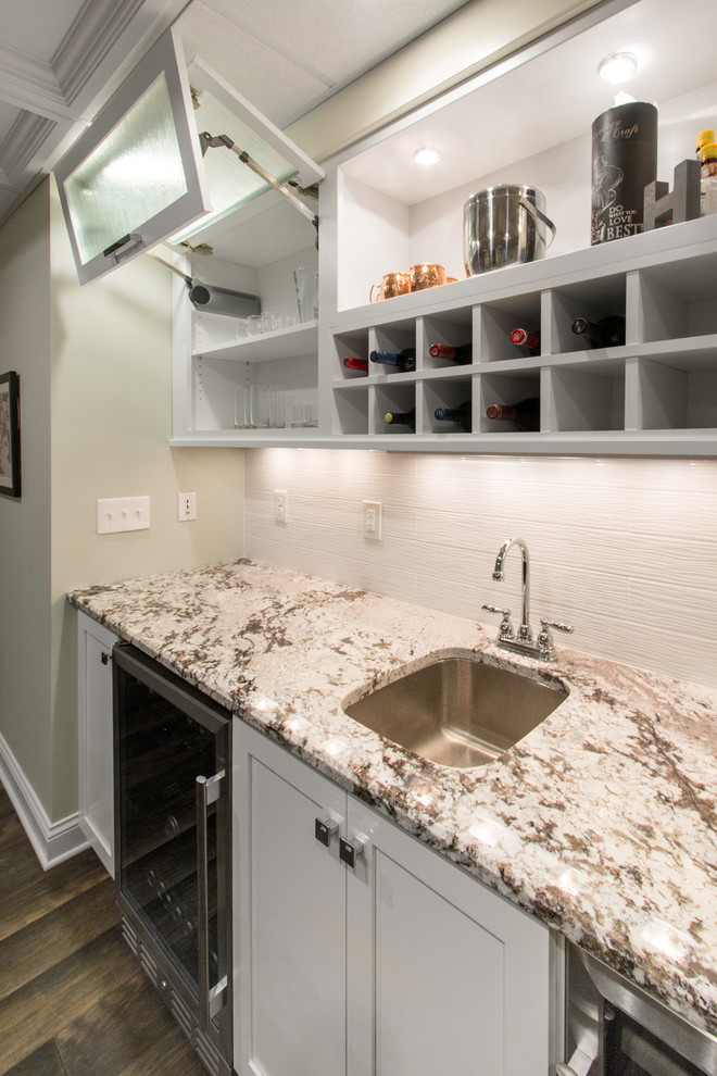 Inspiration for a mid-sized transitional single-wall medium tone wood floor and brown floor wet bar remodel in Milwaukee with an undermount sink, flat-panel cabinets, white cabinets, granite countertops, white backsplash and porcelain backsplash