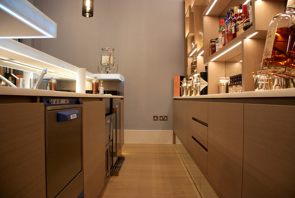 This is an example of a large modern single-wall bar cart in London with a built-in sink, open cabinets, light wood cabinets, onyx worktops, multi-coloured splashback, mirror splashback, light hardwood flooring, grey floors and white worktops.