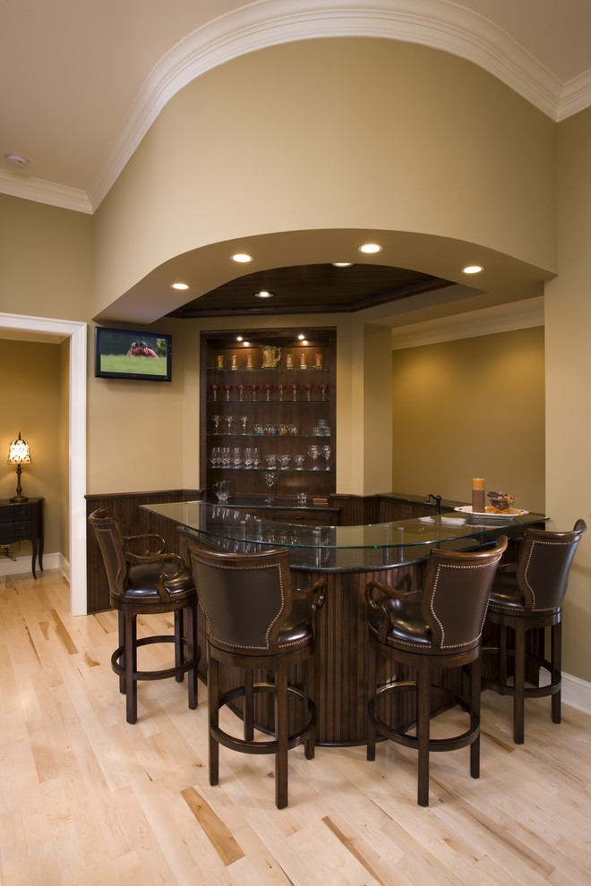 This is an example of a traditional u-shaped breakfast bar in Minneapolis with light hardwood flooring, dark wood cabinets and glass worktops.