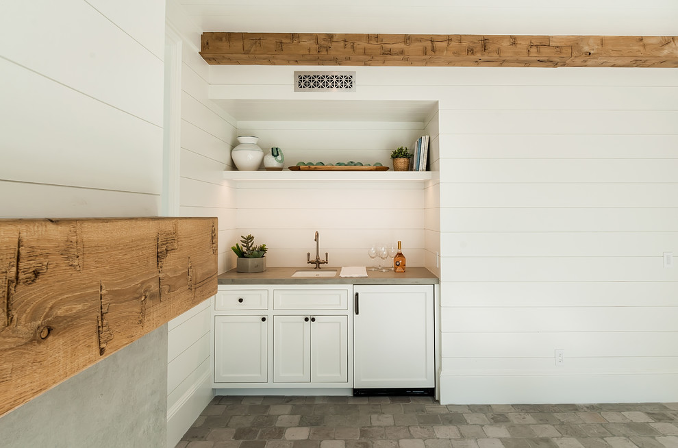 Photo of a large rural single-wall wet bar in Los Angeles with a submerged sink, recessed-panel cabinets, white cabinets, composite countertops, white splashback, limestone flooring, grey floors and grey worktops.