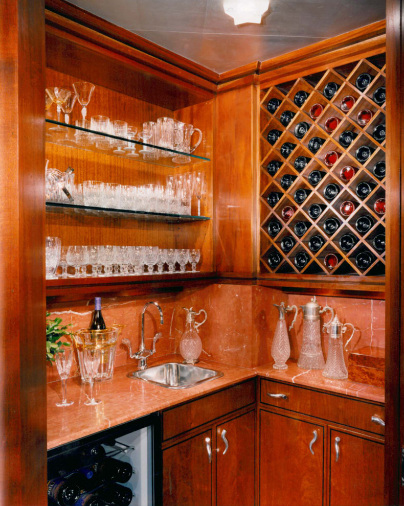 Medium sized traditional l-shaped wet bar in New York with a built-in sink, flat-panel cabinets, dark wood cabinets, orange splashback and stone slab splashback.