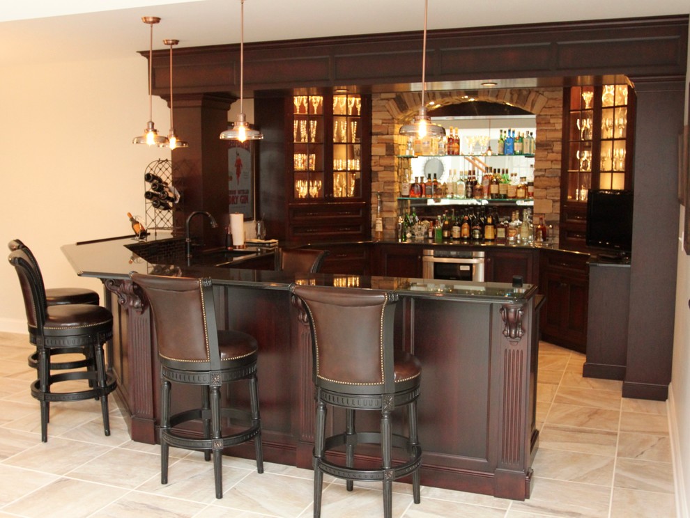 This is an example of a large traditional wet bar with a submerged sink, recessed-panel cabinets, dark wood cabinets, granite worktops, brown splashback, glass tiled splashback and porcelain flooring.