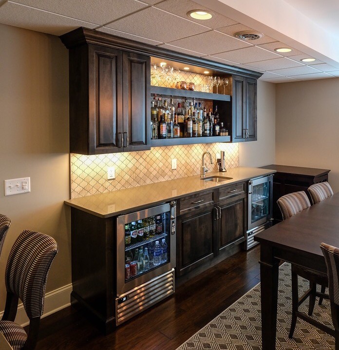 Example of a minimalist single-wall dark wood floor and brown floor wet bar design in Detroit with an undermount sink, raised-panel cabinets, dark wood cabinets, solid surface countertops and stone tile backsplash