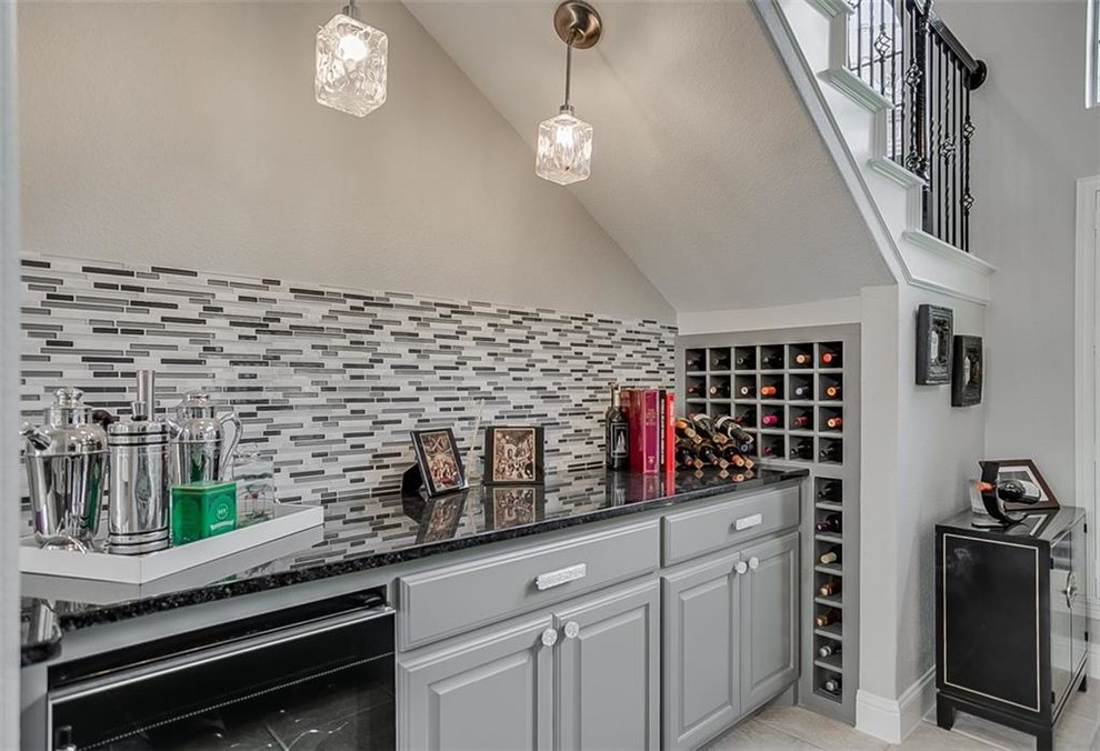 Example of a mid-sized transitional single-wall porcelain tile and beige floor wet bar design in Dallas with raised-panel cabinets, gray cabinets, granite countertops, multicolored backsplash, matchstick tile backsplash and black countertops