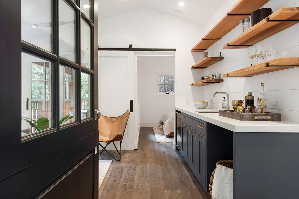 Inspiration for a small transitional galley dark wood floor and brown floor wet bar remodel in San Francisco with blue cabinets, quartzite countertops, white backsplash, wood backsplash, an undermount sink and shaker cabinets