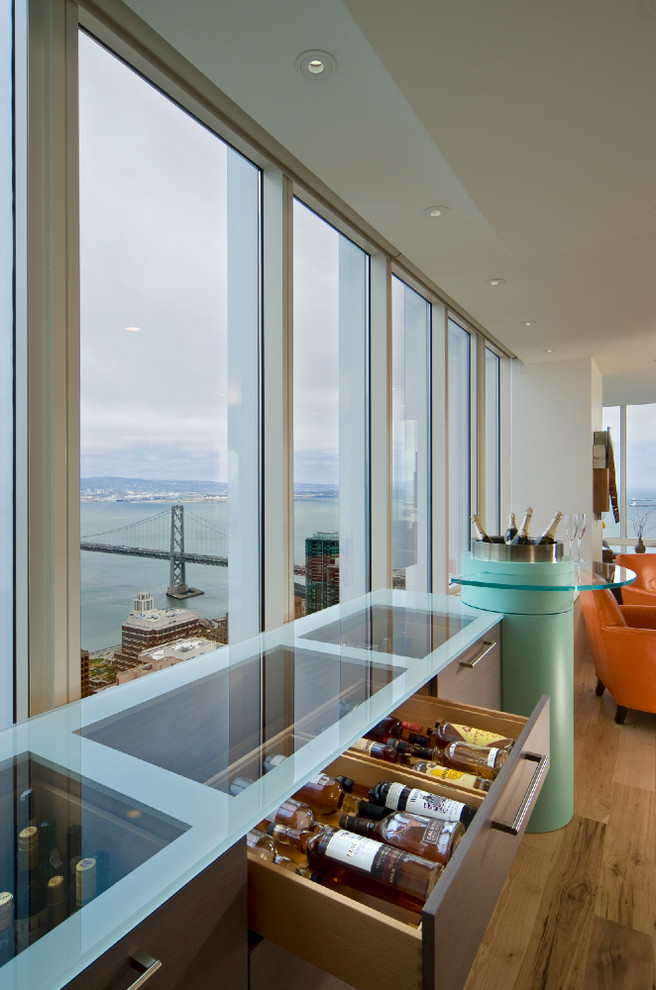 This is an example of a medium sized contemporary single-wall wet bar in San Francisco with flat-panel cabinets, medium wood cabinets, glass worktops and medium hardwood flooring.