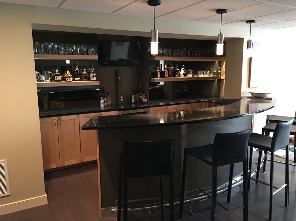 Immagine di un grande bancone bar minimalista con ante in stile shaker, ante in legno chiaro, top in superficie solida, paraspruzzi nero, parquet scuro, pavimento marrone e top nero