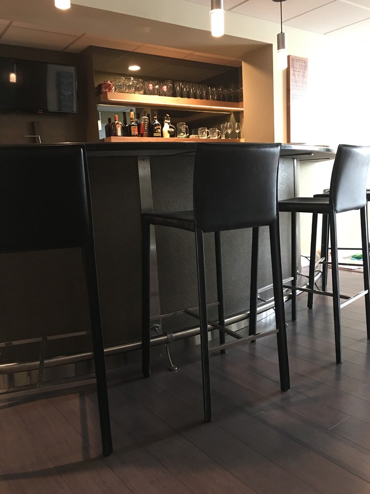 Cette image montre un grand bar de salon minimaliste en U et bois clair avec des tabourets, un placard à porte shaker, un plan de travail en surface solide, une crédence noire, parquet foncé, un sol marron et plan de travail noir.
