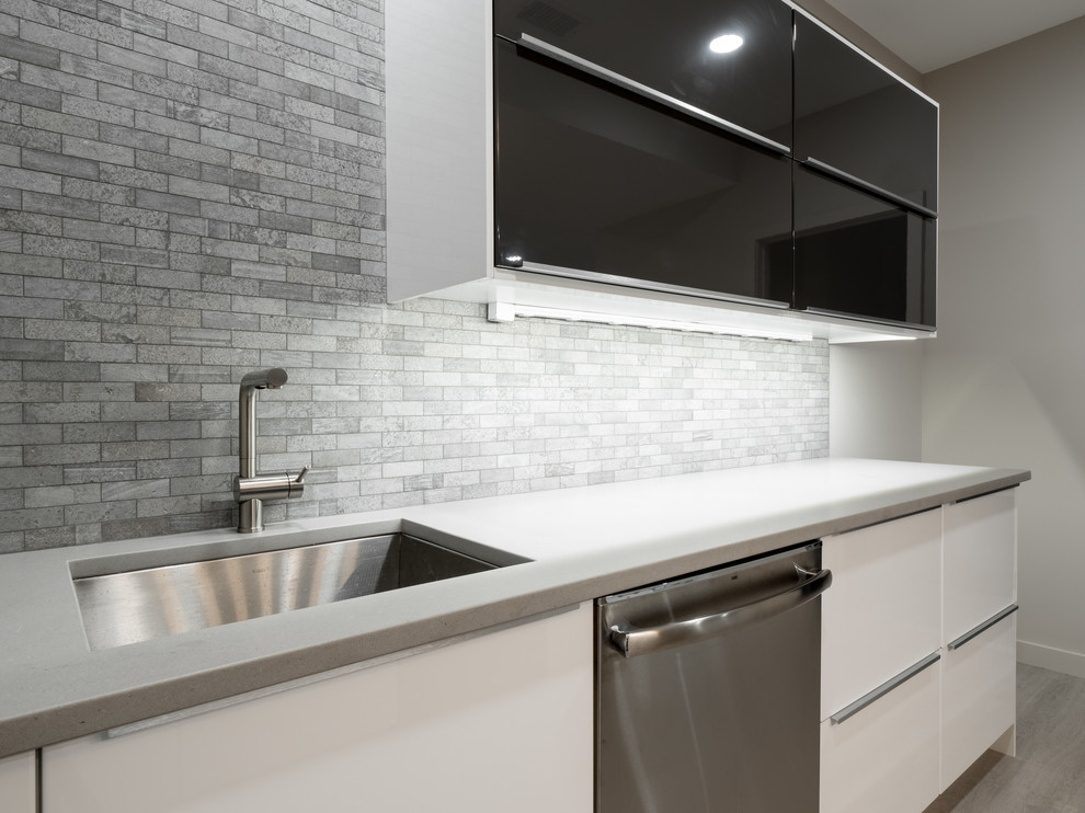 Medium sized contemporary galley wet bar in Other with a submerged sink, flat-panel cabinets, white cabinets, composite countertops, grey splashback, marble splashback, laminate floors, grey floors and white worktops.