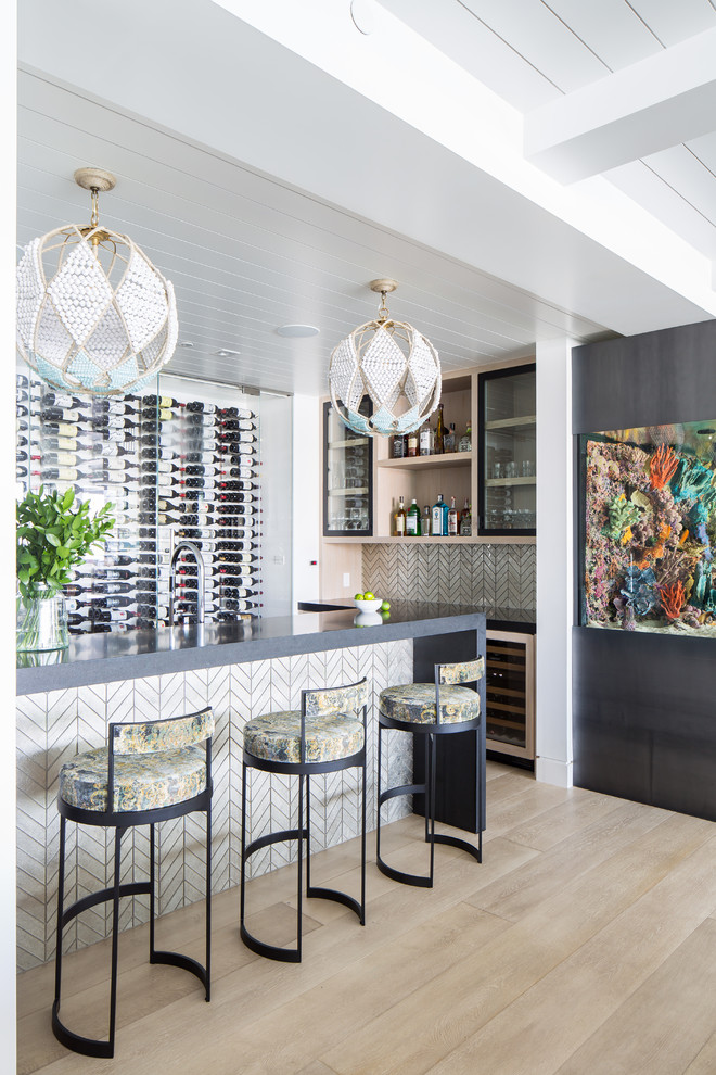 Beach style light wood floor and beige floor seated home bar photo in Orange County with glass-front cabinets, beige backsplash and gray countertops