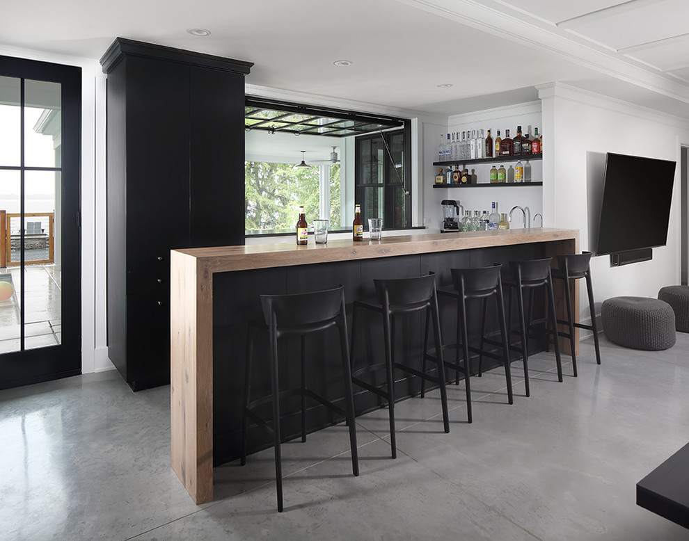 Modelo de bar en casa con barra de bar de estilo de casa de campo con puertas de armario negras, encimera de madera, suelo de cemento y suelo gris