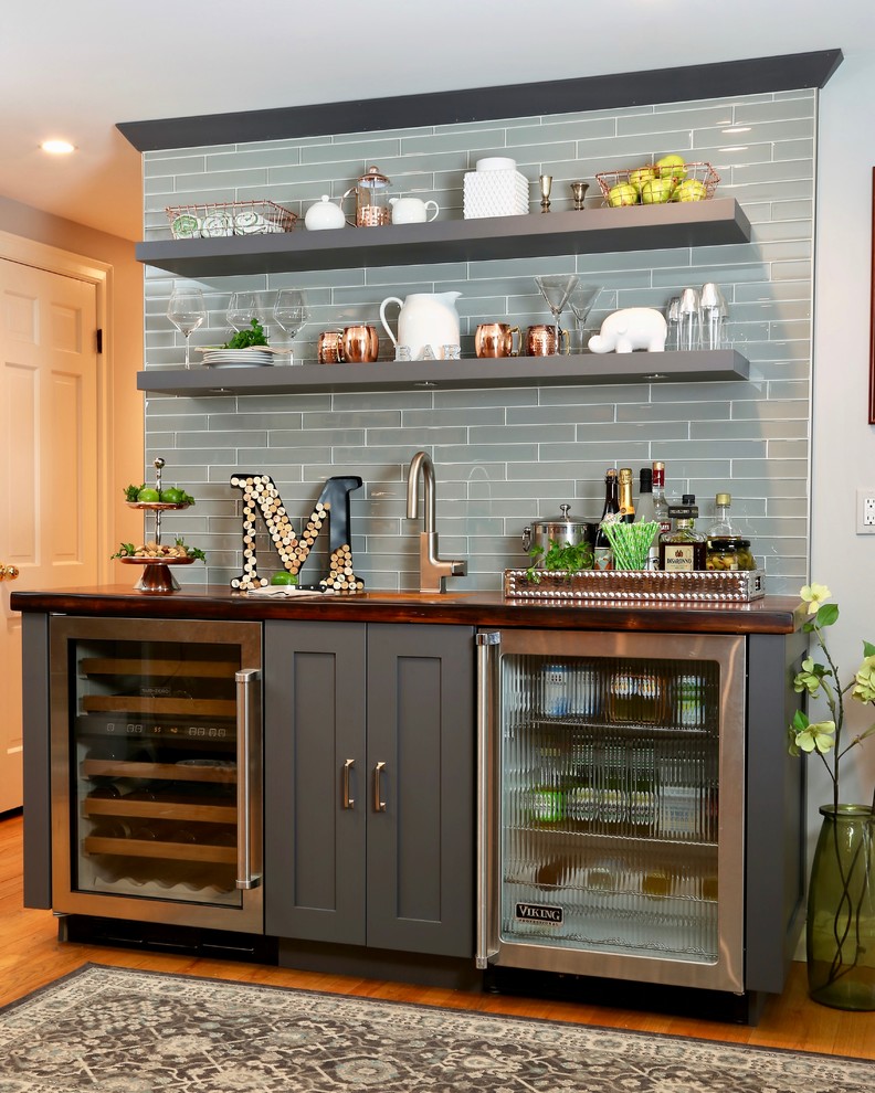 Example of a mid-sized transitional single-wall medium tone wood floor wet bar design in Other with an undermount sink, gray cabinets, wood countertops, gray backsplash, glass tile backsplash, brown countertops and shaker cabinets