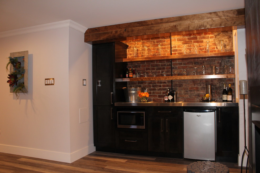 Aménagement d'un bar de salon moderne en bois foncé avec un placard à porte shaker, un plan de travail en inox et une crédence en brique.