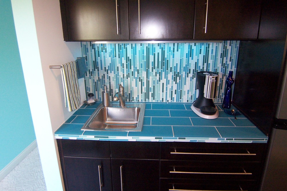 Example of a small minimalist single-wall wet bar design in Cincinnati with a drop-in sink, flat-panel cabinets, black cabinets, tile countertops, blue backsplash and glass tile backsplash
