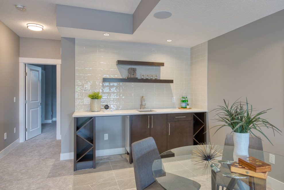 Mid-sized transitional single-wall marble floor and gray floor wet bar photo in Calgary with an undermount sink, flat-panel cabinets, dark wood cabinets, quartzite countertops, gray backsplash, subway tile backsplash and white countertops