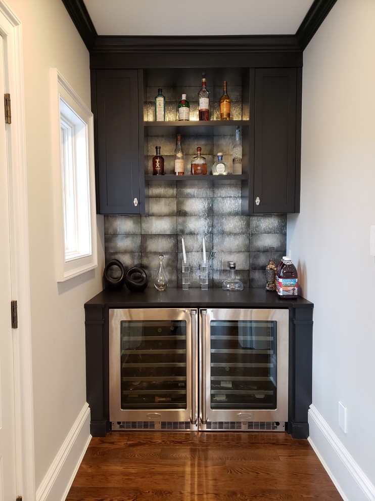 Home bar - transitional single-wall medium tone wood floor and brown floor home bar idea in New York with shaker cabinets, black cabinets, gray backsplash and black countertops