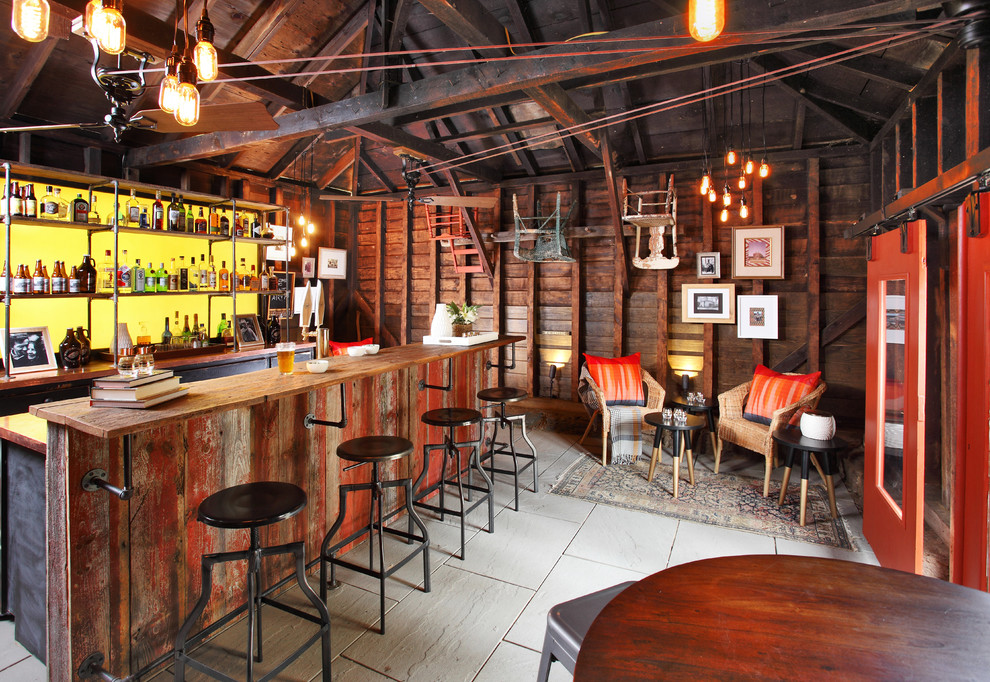 На фото: большой параллельный домашний бар в стиле кантри с барной стойкой, искусственно-состаренными фасадами, деревянной столешницей, полом из керамической плитки, бежевым полом и коричневой столешницей