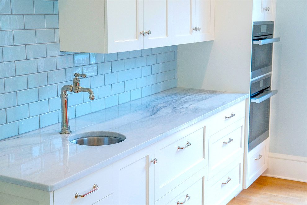 This is an example of a large eclectic single-wall wet bar in Seattle with a submerged sink, recessed-panel cabinets, white cabinets, marble worktops, blue splashback, metro tiled splashback, medium hardwood flooring, brown floors and white worktops.