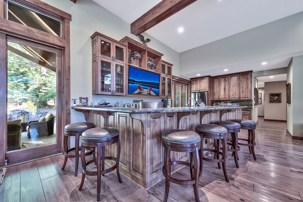 Mid-sized transitional l-shaped medium tone wood floor and multicolored floor seated home bar photo in Other with an undermount sink, glass-front cabinets, medium tone wood cabinets, granite countertops and multicolored countertops
