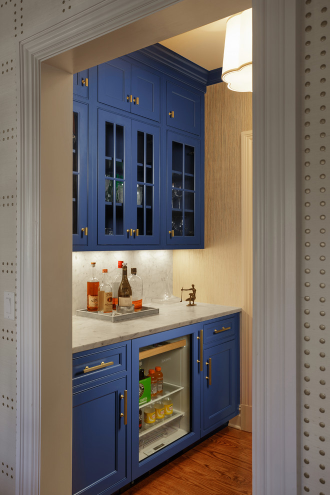 Klassisk inredning av en mellanstor parallell hemmabar med vask, med en undermonterad diskho, luckor med infälld panel, blå skåp, marmorbänkskiva, vitt stänkskydd, stänkskydd i marmor, mellanmörkt trägolv och brunt golv