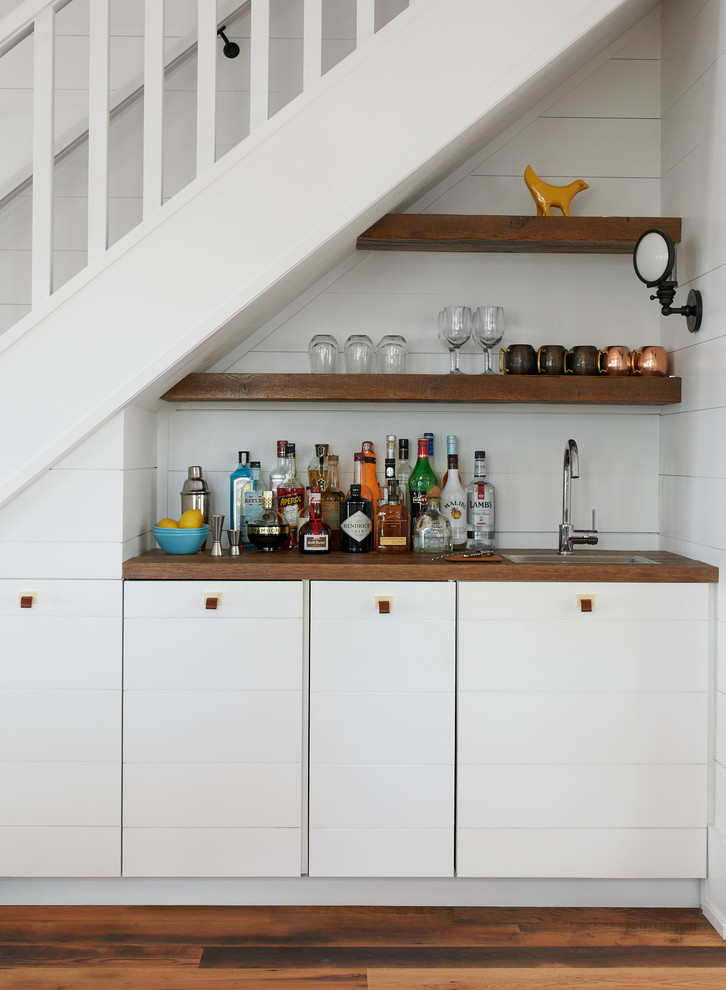 This is an example of a small coastal single-wall wet bar in Toronto with wood worktops, white splashback, medium hardwood flooring, brown floors, brown worktops, flat-panel cabinets and white cabinets.
