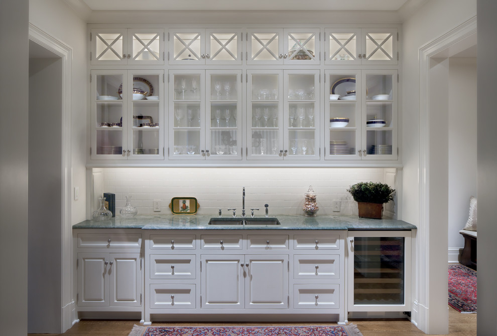 Exempel på en klassisk linjär hemmabar med vask, med en undermonterad diskho, luckor med glaspanel, vita skåp, marmorbänkskiva, vitt stänkskydd och stänkskydd i tunnelbanekakel