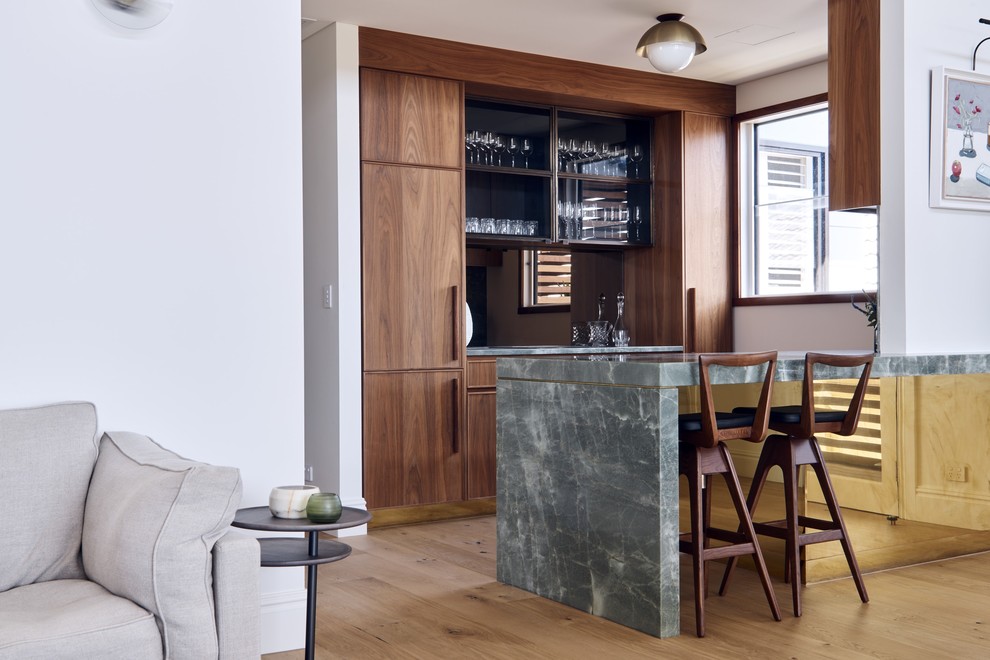 Diseño de bar en casa con barra de bar de galera contemporáneo con armarios con paneles lisos, puertas de armario de madera en tonos medios, suelo de madera en tonos medios, suelo marrón y encimeras grises