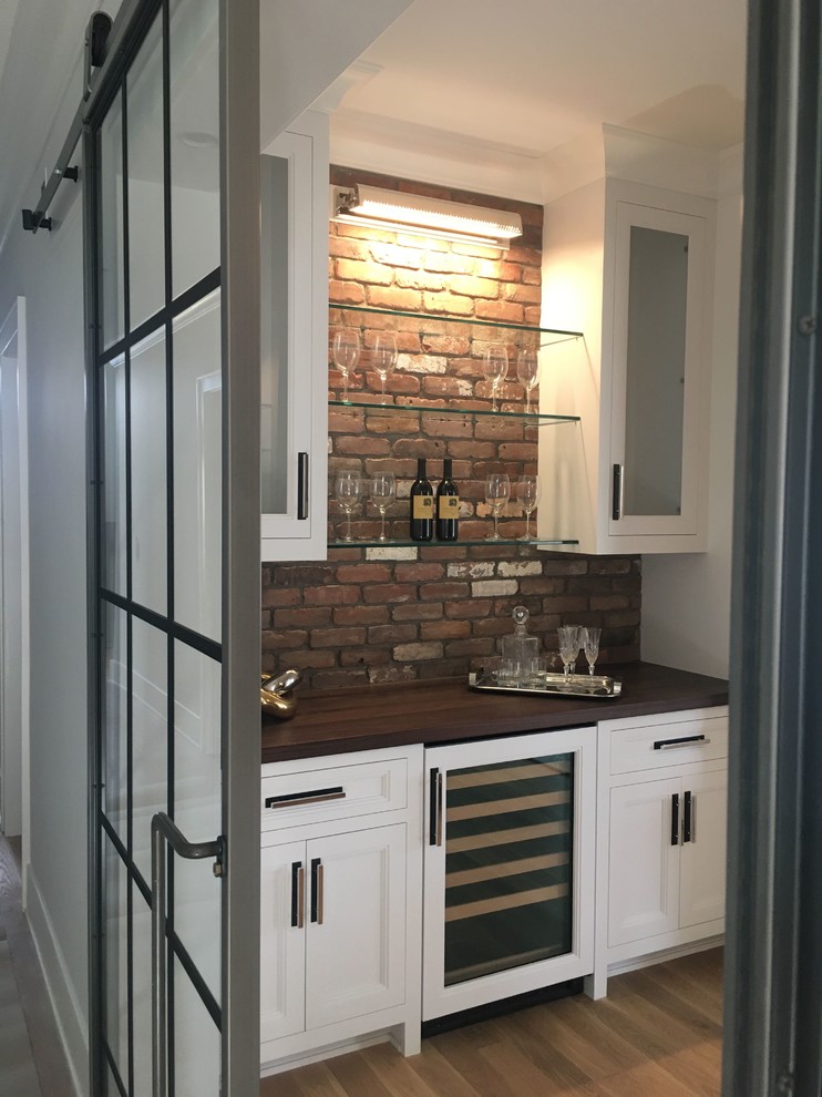 This is an example of a medium sized contemporary single-wall home bar in New York with no sink, glass-front cabinets, white cabinets, wood worktops, red splashback, brick splashback, light hardwood flooring, beige floors and brown worktops.