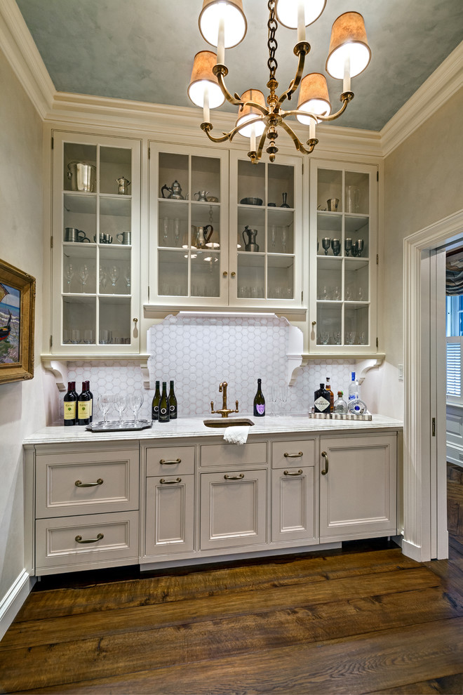 Inspiration for a transitional medium tone wood floor home bar remodel in New York with an undermount sink, glass-front cabinets, white cabinets, granite countertops, gray backsplash and ceramic backsplash