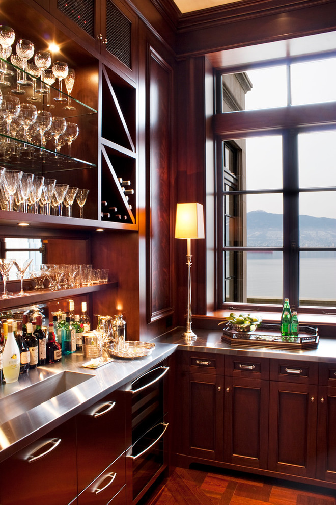 Photo of a classic home bar in Vancouver with an integrated sink, recessed-panel cabinets, dark wood cabinets, stainless steel worktops and dark hardwood flooring.