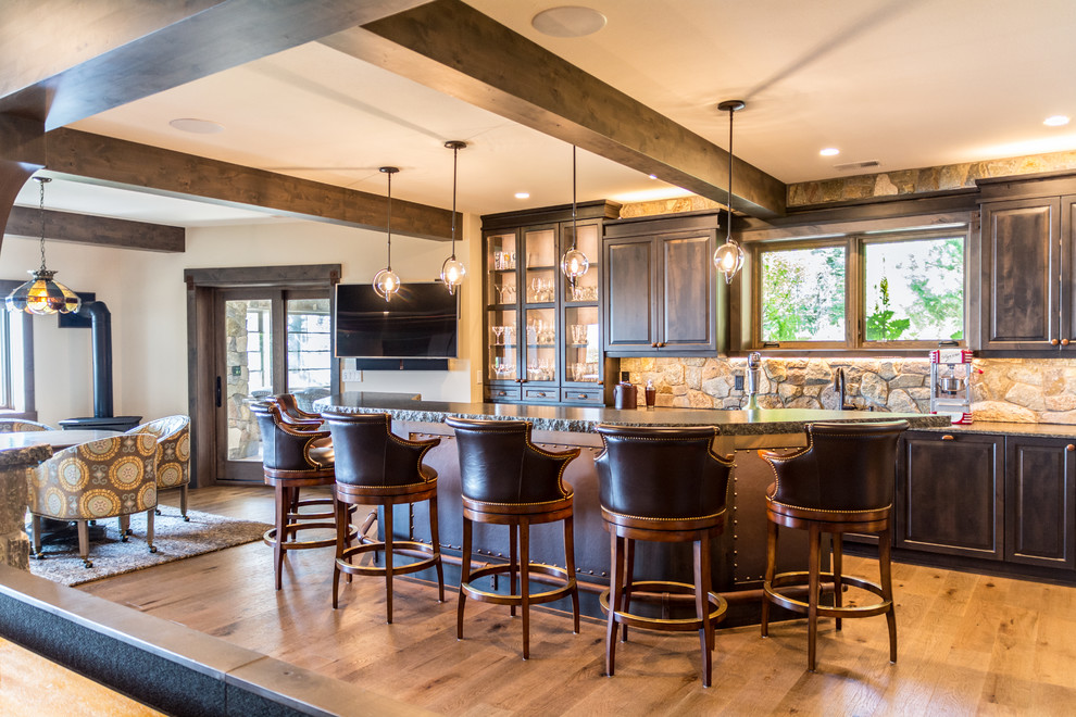 Mountain style galley medium tone wood floor and brown floor wet bar photo in Other with raised-panel cabinets, dark wood cabinets, gray backsplash and gray countertops