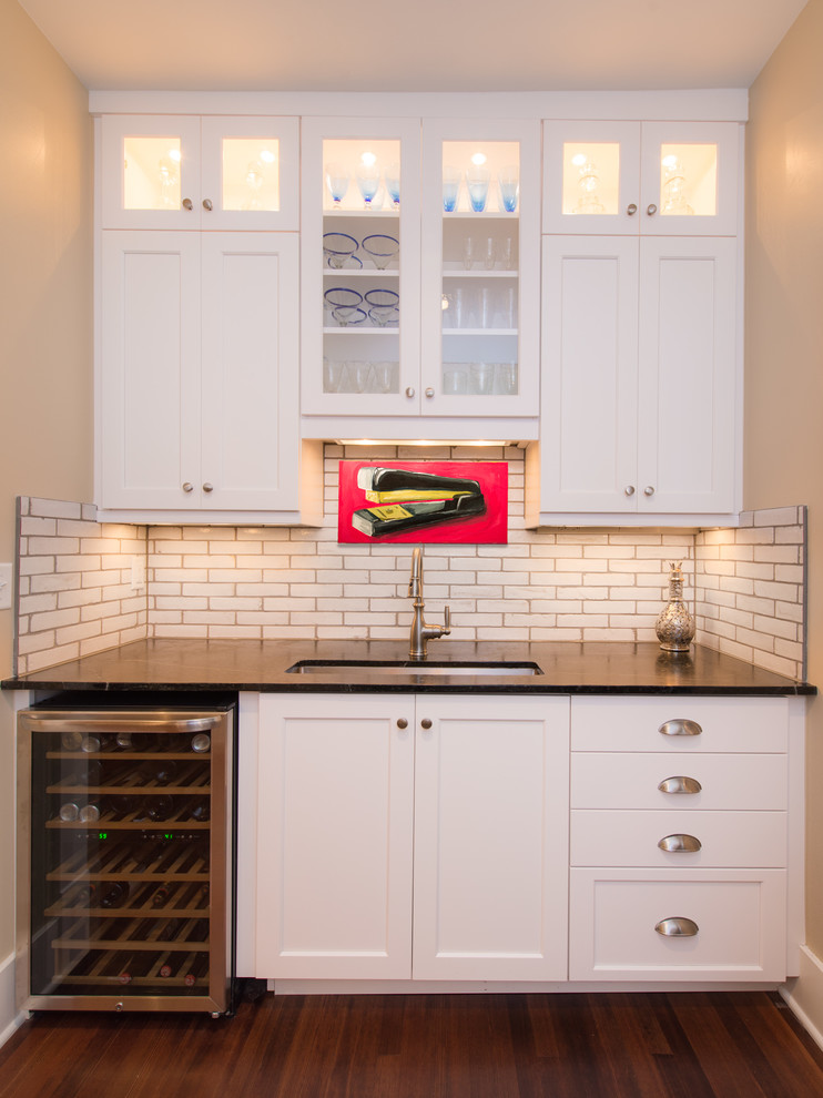 Design ideas for a small classic single-wall wet bar in Denver with a submerged sink, shaker cabinets, white cabinets, white splashback, metro tiled splashback and dark hardwood flooring.