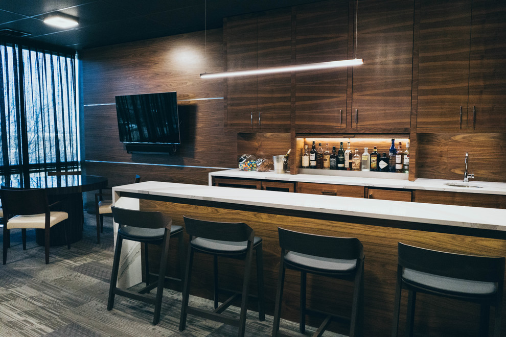 Immagine di un grande angolo bar con lavandino minimalista con lavello sottopiano, ante lisce, ante marroni, top in marmo, paraspruzzi in legno, moquette e pavimento grigio