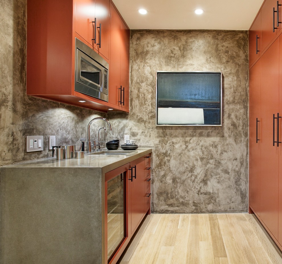 This is an example of a small contemporary single-wall home bar in San Francisco with flat-panel cabinets, light hardwood flooring, beige floors, a submerged sink and orange cabinets.