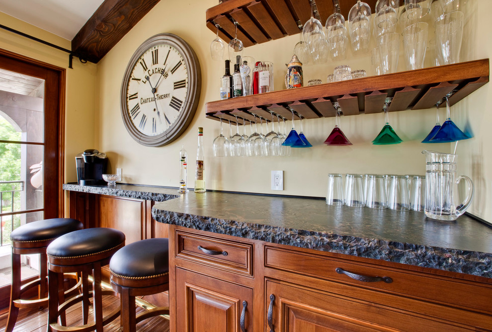 Ejemplo de bar en casa con barra de bar lineal mediterráneo con armarios con paneles con relieve y puertas de armario de madera oscura