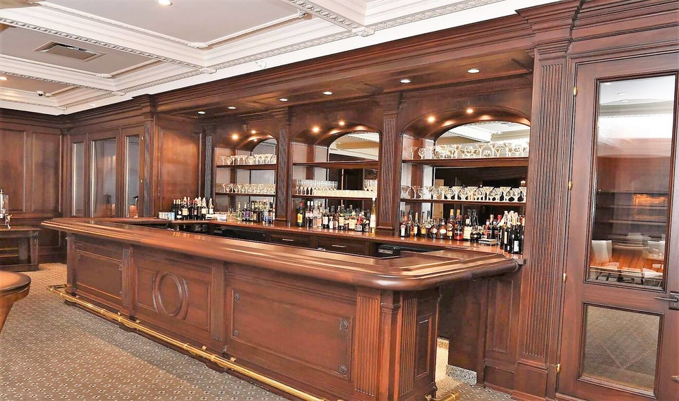 Aménagement d'un grand bar de salon classique en U avec des tabourets, un placard avec porte à panneau encastré, des portes de placard marrons, un plan de travail en granite, moquette et un sol gris.