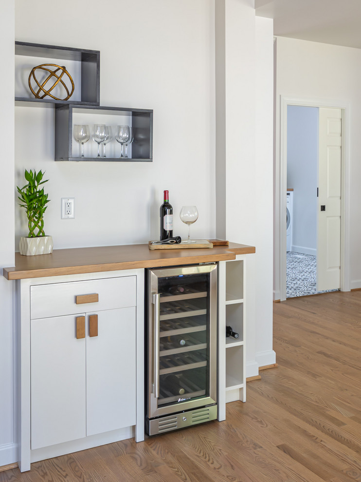 Photo of a small country single-wall home bar in Raleigh with flat-panel cabinets, white cabinets, wood worktops and light hardwood flooring.