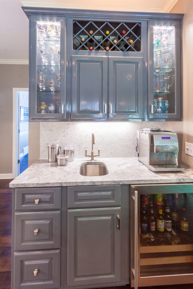 Example of a mid-sized transitional l-shaped dark wood floor and brown floor home bar design in Other with an undermount sink, raised-panel cabinets, white cabinets, granite countertops, white backsplash and ceramic backsplash