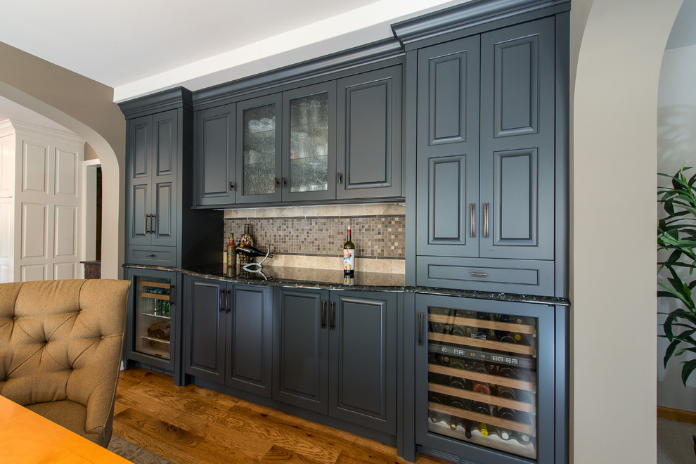 Wet bar - mid-sized contemporary single-wall medium tone wood floor and brown floor wet bar idea in Minneapolis with glass-front cabinets, gray cabinets, granite countertops, beige backsplash, stone tile backsplash and no sink