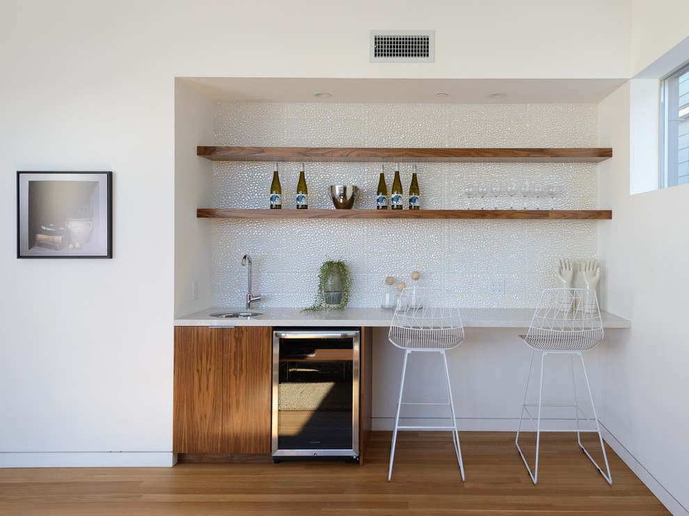 Einzeilige, Kleine Moderne Hausbar mit braunem Holzboden, Bartheke, flächenbündigen Schrankfronten, dunklen Holzschränken, Küchenrückwand in Weiß und braunem Boden in Los Angeles
