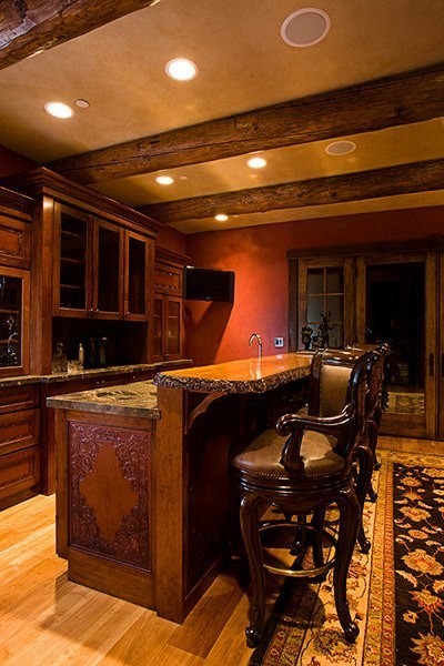 Diseño de bar en casa con barra de bar de estilo americano grande con armarios con paneles empotrados, puertas de armario de madera oscura y encimera de madera
