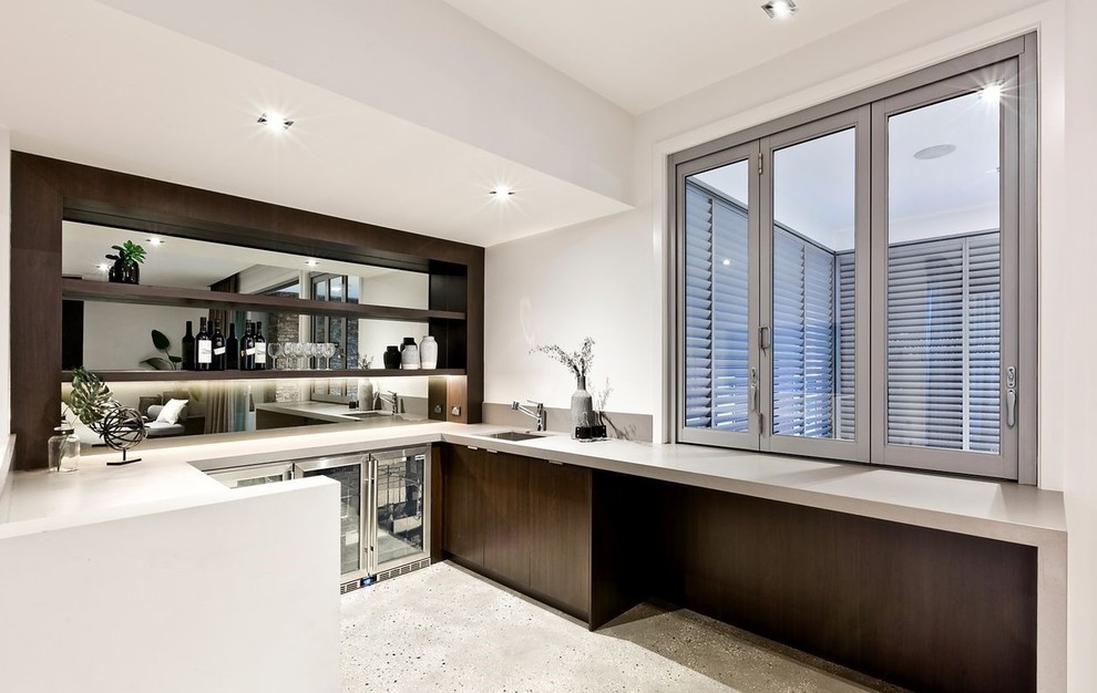 Large modern u-shaped wet bar in Melbourne with a submerged sink, flat-panel cabinets, dark wood cabinets, engineered stone countertops, mirror splashback, concrete flooring, grey floors and grey worktops.